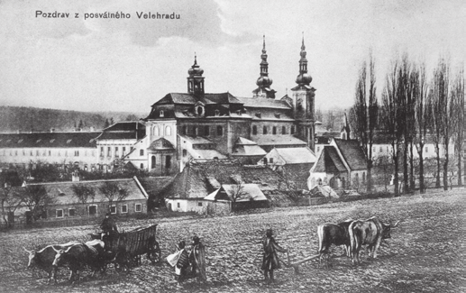 kostela a střechami někdejšího kláštera, zasazeného do zeleně a střech vesnice. Vše z jedné strany lemuje vzrostlý Háj a v dáli šedivá silueta Bílých Karpat.