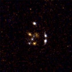 Zvětšit obrázek Trojice bližších galaxií (oranžové) ve vzdálenosti sedm miliard světelných let rozdělí obraz jedenáct miliard světelných let vzdálené galaxie do šesti bílých obrazů (zdroj Hubble