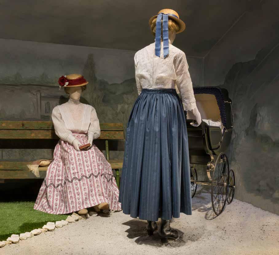 UPLATNĚNÍ DOBOVÉ MÓDY V PROSTŘEDÍ ROŽNOVA POD RADHOŠTĚM, rekonstrukce situace, Rožnov pod Radhoštěm, okolo 1900 ŽENA SEDÍCÍ NA LAVIČCE Klobouk slaměný s červenou krinolínou a textilními květinami,