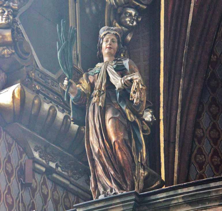 Socha sv. Ludmily na balustrádě varhanní kruchty Sv. Ludmila stojí hned jako první v řadě zleva, v ruce s atributem šálu, jímž byla uškrcena.