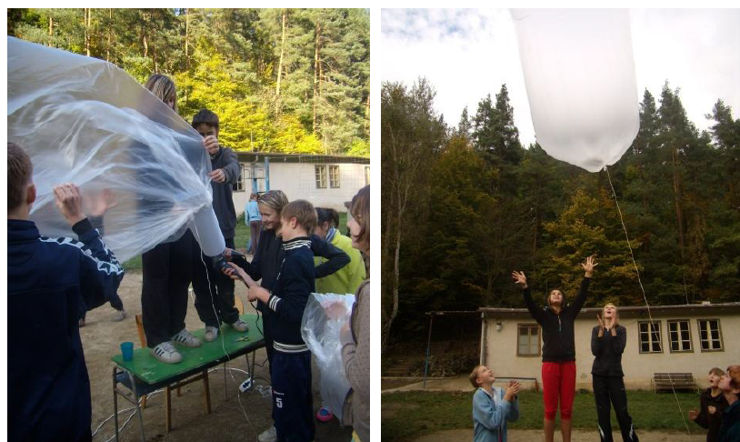 Balón ve spodní části přivážeme ke klubku provázku. Pak nasadíme balón na trubku. Balón u trubky předržujeme. Přes trubku foukáme dovnitř horký vzduch 1 až 2 fény.
