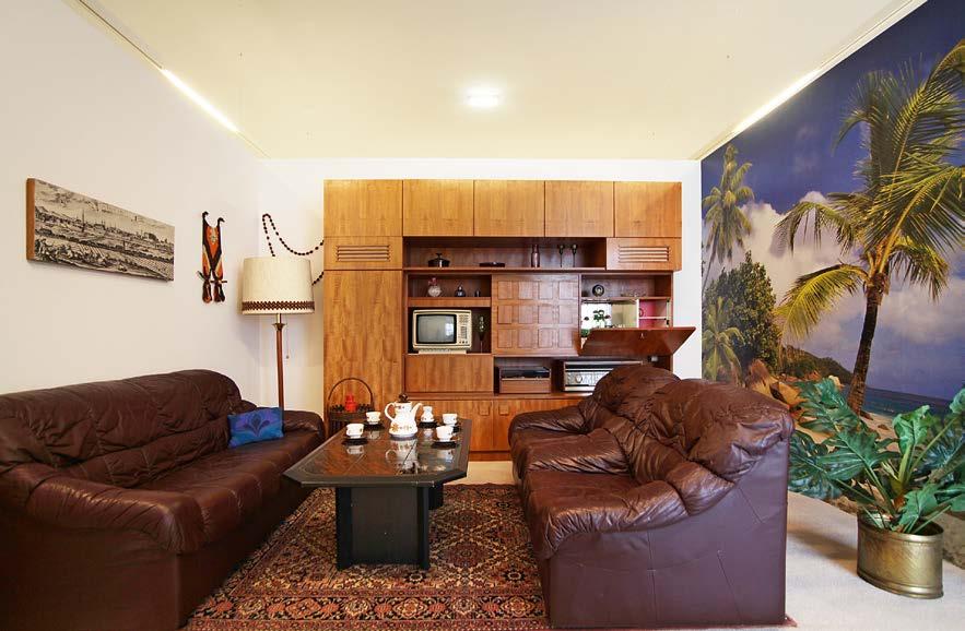 Obytná stěna s televizí, kobercem, fototapetou a těžká sedací souprava charakterizují obytný prostor ze 70. let.