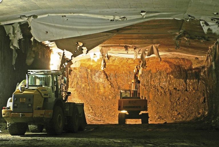 Na konstrukčních podzemních stěnách, tvořících definitivní opěrové části ostění tunelu, se realizuje z povrchu (případně z nižší odtěžené úrovně) stropní konstrukce tunelu, která se následně zasype