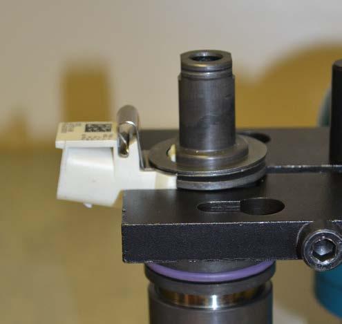 Utáhněte upevnění pomocí šestihranného klíče 6,0 mm při zajištění opření ramene vstřikovače v demontážním přípravku.
