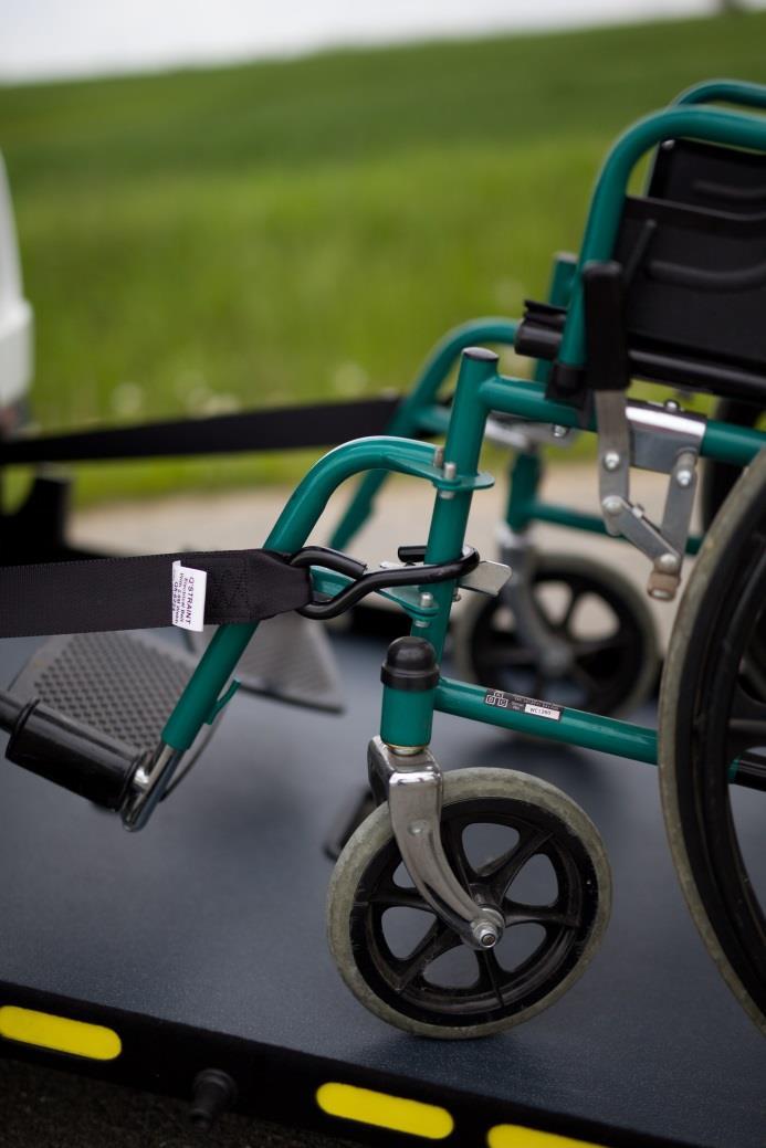 Obrázek 9 Vytáhněte pásy ven z vozidla a upevněte je za rám v přední části invalidního vozíku. Nikdy nepřipevňujte pásy za stupačky invalidního vozíku.