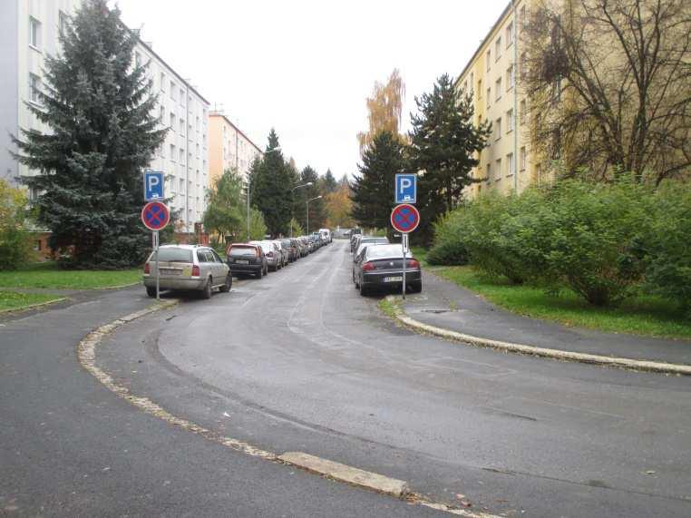 komunikace, přičemž vozidla částečně parkují na chodníku.