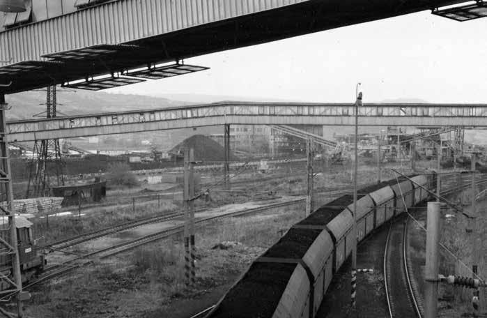 Přírodověda Odbytové místo v Trmicích. V pozadí vlevo depo uhlí, v pozadí vpravo objekt hrubé drtírny, vodorovně středem fotografie vede zakrytý most, ve kterém je umístěn lanopásový dopravník.