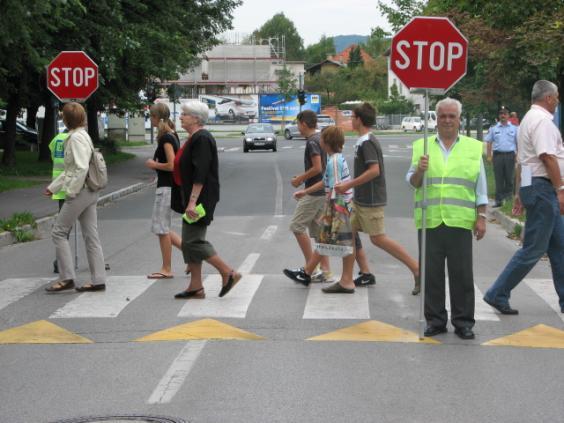 of road, nearer to the left edge, using the stop sign to signal to the pedestrians that it is forbidden to cross road.
