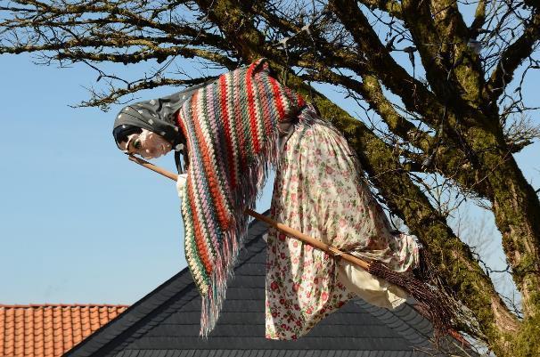 Na hlavě má klobouk. Je krásný slunečný den. V ruce drží odkvetlou pampelišku. V ruce drží koště.